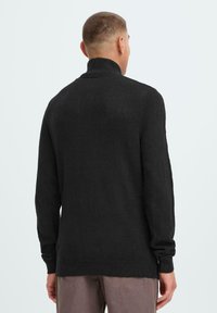 Black turtleneck sweater made of soft fabric, featuring long sleeves and a ribbed hem, viewed from the back against a light background.
