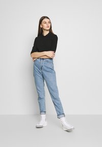Svart polo-skjorte med middels lange ermer, parret med høyhøyde lyseblå jeans og hvite joggesko med mønstret såle.
