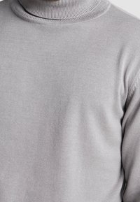 Ljust grått polokrage-tröja med ribbad krage och slät textur. Nærbild som visar det mjuka stickade tyget och sömlösa designen.