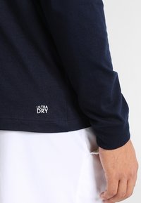 Camiseta de manga larga color azul marino con textura suave, que presenta el logo blanco "ULTRA DRY" cerca del dobladillo y un diseño de ajuste holgado.