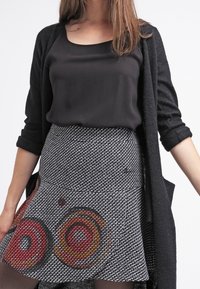 Haut en satin noir associé à une jupe évasée à motifs avec des motifs circulaires rouges et oranges sur un fond noir et blanc. Tissu texturé.