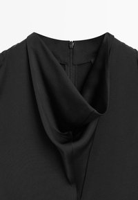 Zwarte kleding met een gedrapeerde, gevouwen halslijn en een zichtbare zwarte rits in het midden achteraan.