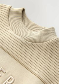 Beige mikina s texturovaným žebrovaným výstřihem, s hladkým tělem a vyšívaným nápisem na přední straně. Měkký materiál z bavlněné směsi.