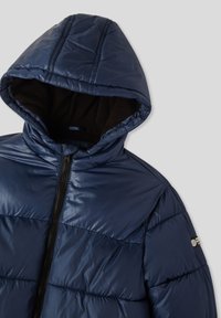Granatowa kurtka puchowa z pikowanym wzorem, podszewką w kapturze oraz czarnym zamkiem błyskawicznym z akcentem logo na rękawie. Miękka tekstura.