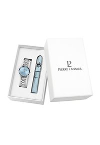 Reloj de acero inoxidable con un dial azul claro, marcadores de hora plateados y una correa de cuero azul a juego, presentado en una caja blanca con el logo.