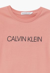 Różowy bawełniany T-shirt z okrągłym dekoltem i krótkimi rękawami, z napisem "CALVIN KLEIN" wytłoczonym pogrubionymi czarnymi literami na piersi.