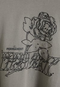 Μαύρο σχέδιο με γραμμή ενός τριαντάφυλλου με φύλλα σε γκρι ύφασμα, συνοδευόμενο από το κείμενο "On a PERMANENT" πάνω από στυλιζαρισμένο, μερικώς κρυμμένο κείμενο από κάτω.