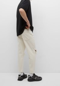 Valkoiset revityt farkut rentolla istuvuudella, yhdistetty mustaan lyhythihaiseen paitaan. Päällä mustat urheilukengät ja valkoiset sukat.