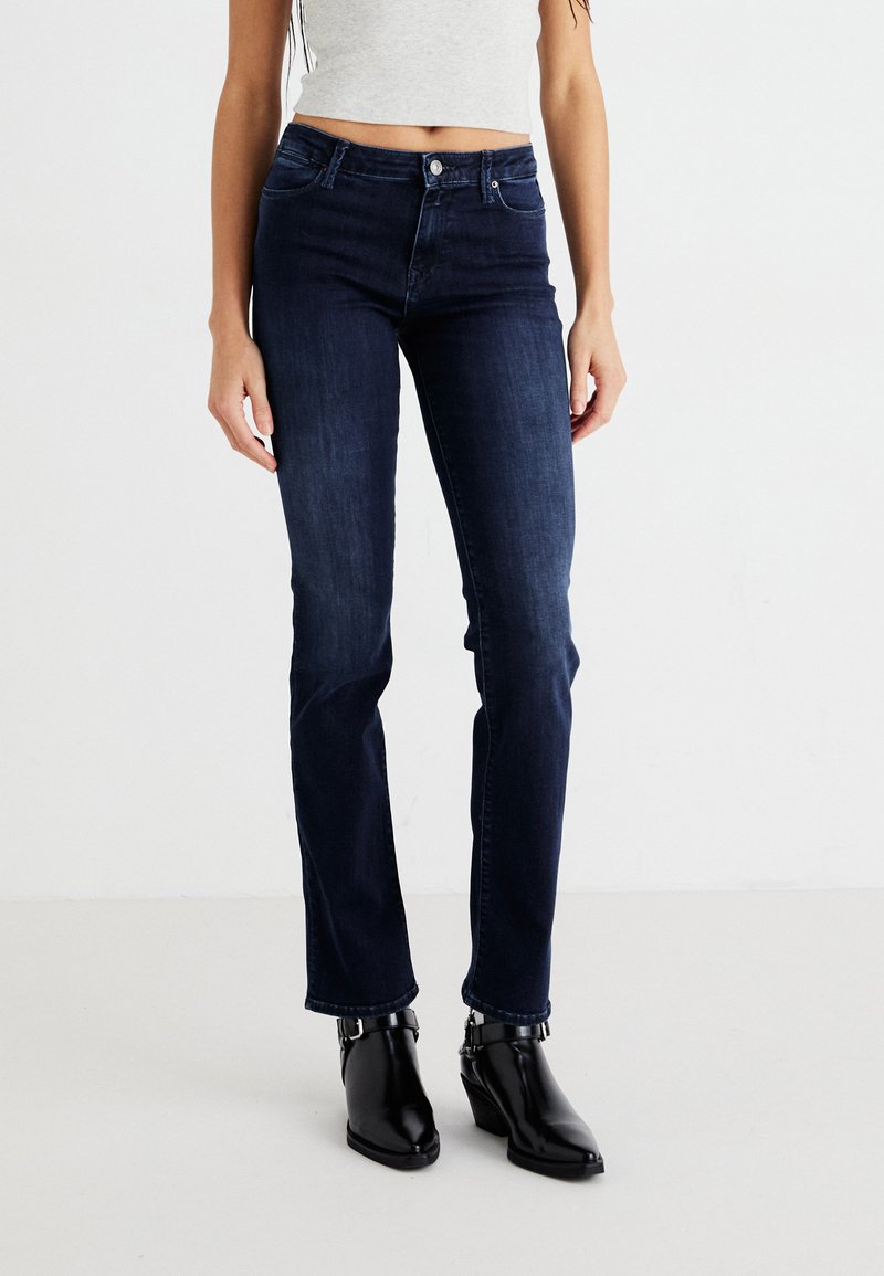 Temno pranje jeans hlače s ravnim krojem, z zapiranjem na gumb in dvema sprednjima žepoma. Združene z črnimi gležnjarji.