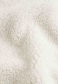 Vitt fleecetyg med en mjuk, fluffig textur. Ytan har upphöjda, rundade fibrer som skapar ett mysigt utseende.