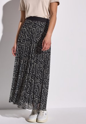 Schwarzer, gefalteter Rock mit einem grauen abstrakten Muster, ausgestattet mit einem breiten elastischen Bund. Kombiniert mit weißen Sneakers auf einer hellen Oberfläche.
