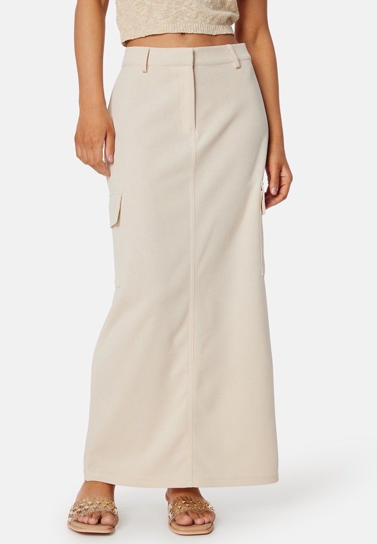 Beige maxi-jurk met een rechte snit, zijzakken en een gladde, textuurstof. Draagt met sierlijke platte sandalen.