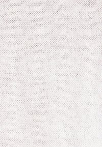 Gros plan d’un tissu blanc tricoté montrant des mailles entrelacées détaillées dans un motif uniforme.