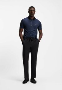 Kobaltblaues Poloshirt mit einem schwarzen Kragen und einem dezenten Logo; kombiniert mit schwarzen Hosen und schwarzen Schuhen. Glatte Textur, moderne Passform.