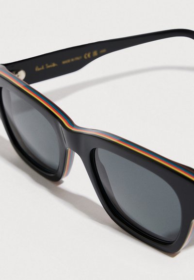 Gafas de sol negras con lentes grises; presentan un detalle de rayas multicolores a lo largo de la montura. El material parece brillante con una forma geométrica moderna.