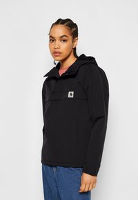 Giacca nera impermeabile con cappuccio, tasca frontale con zip e patch con logo. Presenta un fit rilassato e un tessuto testurizzato.