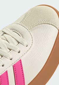 Baskets en cuir blanc avec des rayures roses, un bout en daim beige, des lacets blancs et une semelle en caoutchouc marron.