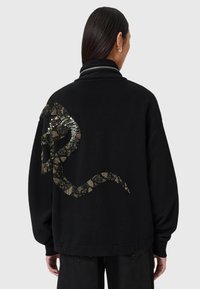 Felpa nera oversize con un design testurizzato a forma di serpente in paillettes dorate e nere sul retro, dotata di un colletto alto e una vestibilità rilassata.