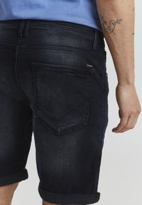 Mørke denimshorts med rullet kant, med en baklomme med en unik form, subtile sømdetaljer, og en liten etikett.
