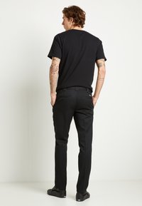 Maglietta nera a maniche corte, in cotone, abbinata a pantaloni neri con tasche laterali e tasche posteriori con bottone, indossati con sneaker nere.