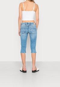 Pantalones capri de mezclilla azul claro con diseño entallado y dobladillo remangado, que cuentan con bolsillos traseros y una etiqueta en la pretina.