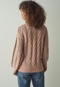 Kabelstrickpullover in Hellpink mit geripptem Saum. Verfügt über ein offenes Strickdetail an den Ärmeln und hat eine mittelgroße, lockere Passform. Kombiniert mit dunklen Jeans.
