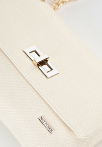 Handtasche aus cremefarbenem Material mit goldfarbenem rechteckigem Verschluss und kleinem Metallschilder "WITTCHEN" auf der Vorderklappe.