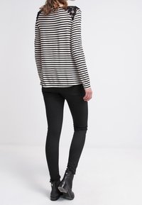 Randig långärmad topp i svart och vitt bomull med spetsdetaljer på axlarna, kombinerad med svarta skinny jeans och ankelkängor.