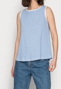 Ärmös blå och vit randig topp med rund halsringning, tillverkad av lättviktsmaterial, tillsammans med högmidjade jeans.