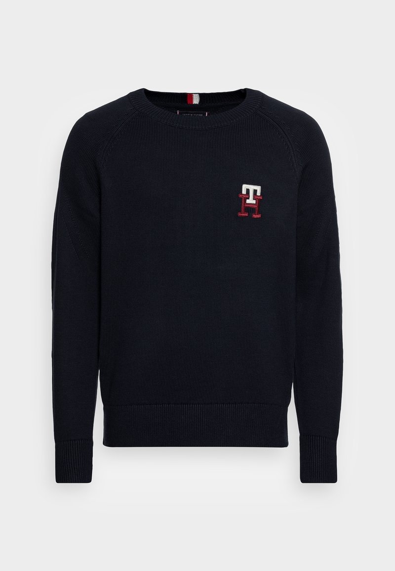 Marineblauwe gebreide trui met geribbelde manchetten en zoom. Voorzien van een klein geborduurd logo in wit en rood op de linkerborst. Rondhals ontwerp.