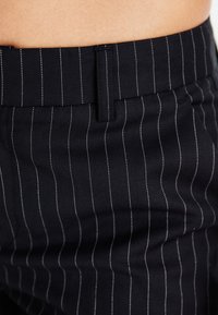Black pinstriped pants with a smooth texture, featuring thin white stripes and a structured waistband. Tailored design emphasizes fit.
