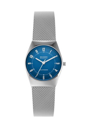 Reloj con correa de malla plateada, esfera azul, números blancos, tres agujas y logo "Skagen Denmark", indicado como alimentado por energía solar.