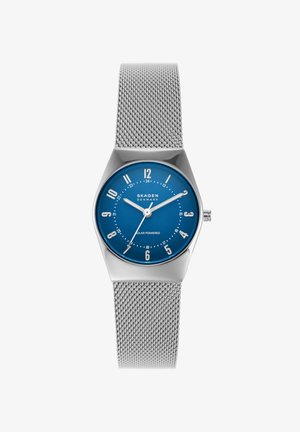 Reloj con correa de malla plateada, esfera azul, números blancos, tres agujas y logo "Skagen Denmark", indicado como alimentado por energía solar.