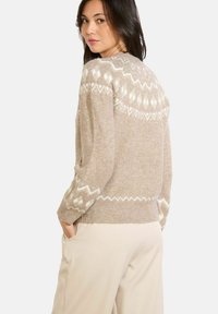 Beige Strickpullover mit weißen geometrischen Mustern. Lange Ärmel, gerippte Bündchen und Saum, weiche Textur, lässige Passform, hoher Kragen.