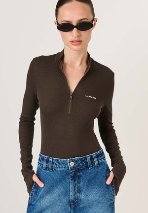 Ruda, briaunuota, ilgomis rankovėmis palaidinė su užtrauktuku ant apykaklės, derinama su šviesiai mėlynais, aukšto liemens džinsiniais šortais. Matomų raštų ar akcentų nėra.