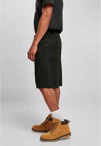 Sorte bomuldsshorts med lige snit, udstyret med to baglommer og synlige stikninger, parret med tanfarvede snørebåndsstøvler.