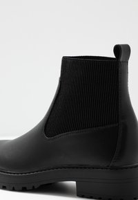 Botín negro que cuenta con un cuerpo de cuero suave y un panel elástico acanalado. La suela es gruesa y resistente, con un patrón de agarre texturizado.