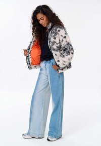 Falošná kožušinová bomber bunda s čierno-bielym kvetinovým vzorom, oranžové podšívka; spárovaná s širokými svetlomodrými denimovými džínsami. Biele tenisky.