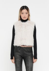 Gilet en fausse fourrure rose clair avec un col montant, courte longueur et surface texturée, associé à un haut noir à manches longues et un pantalon foncé.