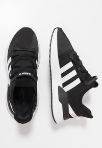 Svartvita Adidas-sneakers med tre vita ränder, svarta snören och tjocka vita sulor, visade från både ovan- och sidovy.