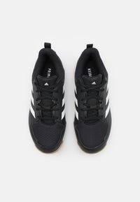 Zwarte sportschoenen met een bovenwerk van mesh, voorzien van drie witte strepen aan de zijkant, een gestructureerde neuskap en een zool van gumrubber.
