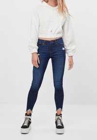 Beskuren vit hoodies med texturerad tyg, kombinerad med mörkblå tighta jeans med slitna detaljer, bärs med svarta plattformssneakers.