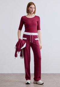 Μαύρο αθλητικό σετ που περιλαμβάνει εφαρμοστό τοπ με μανίκια τριών τετάρτων και φαρδιά παντελόνια με πλαϊνές τσέπες, τονισμένο με λευκές λεπτομέρειες και κορδόνι στη μέση.