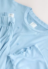 Lys blå bomuldssovetøjssæt bestående af en skjorte med stjerneaccents og matchende bukser med elastisk talje. Blød, let tekstur.