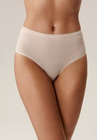 Beżowa, wysokodopasowana bielizna wykonana z gładkiego, elastycznego materiału z subtelnymi szwami oraz małą metką z logo na pasku w talii.
