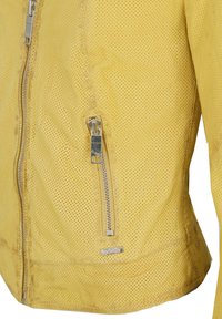 Gele leren jas met perforaties, verticale zilveren ritszak en ritssluiting aan de voorkant.