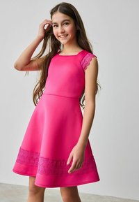 Rotes Kleid mit quadratischer Ausschnitt, strukturierten Spitzeakzenten an den Schultern und einer floralen Spitzenborte am Saum. A-Linie-Silhouette.