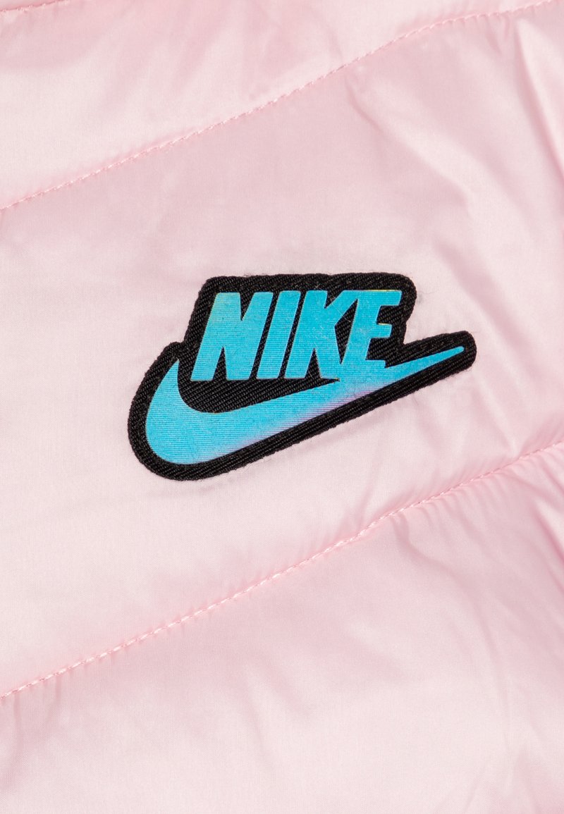 Chaqueta acolchada rosa con el logo negro de Nike. El material es suave y brillante, con un swoosh turquesa. Presenta un sutil cosido diagonal.
