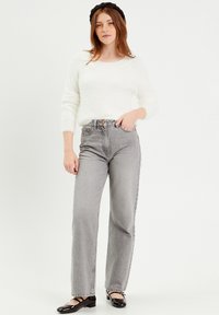 Jean gris taille haute au design droit, associés à un pull blanc duveteux et des chaussures Mary Jane noires.