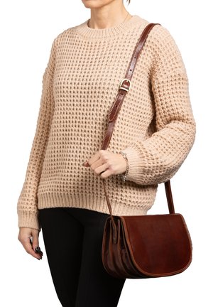 Borsa a spalla in pelle marrone con una patta curva, finitura testurizzata e tracolla regolabile, indossata su un maglione beige a maglia.